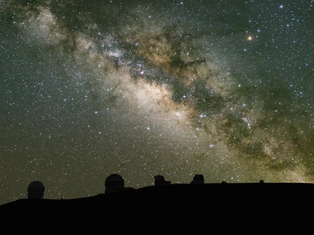 Starry night sky with Milky Way and observatory domes silhouetted.