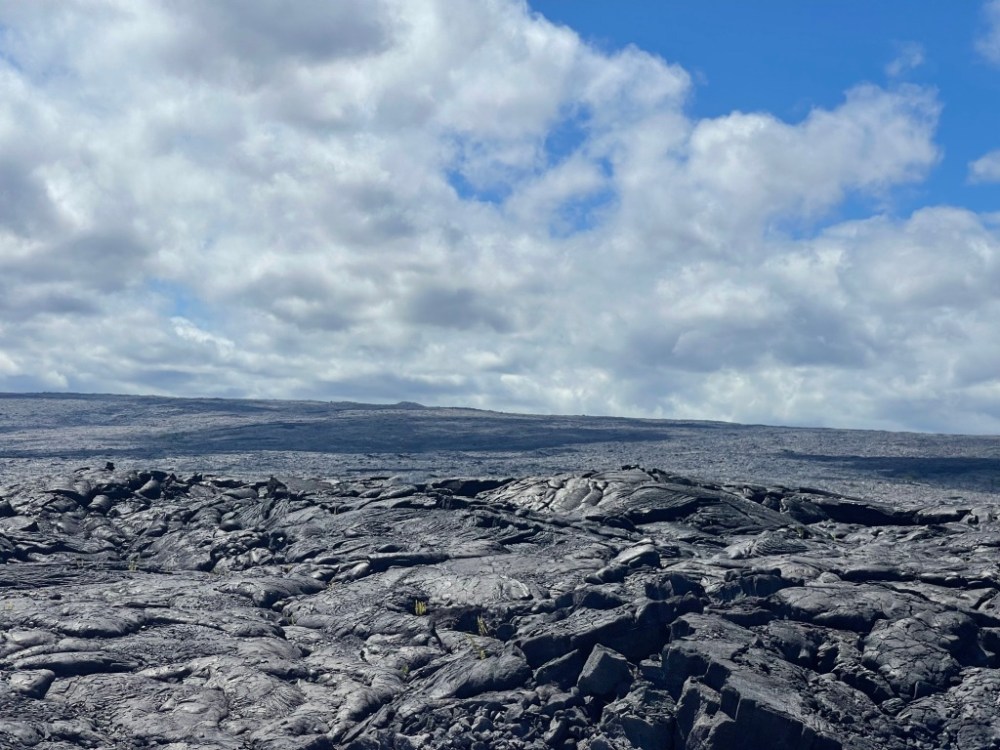 Landscape of dark volcanic rock under a cloudy blue sky.