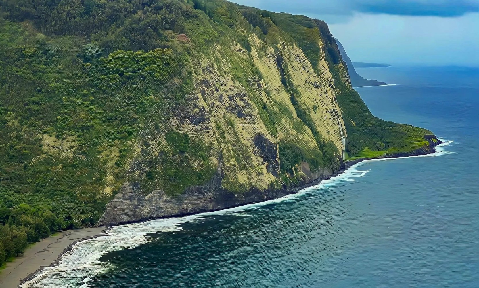 Steep, green cliffside next to ocean with waves crashing on a narrow strip of sandy beach.