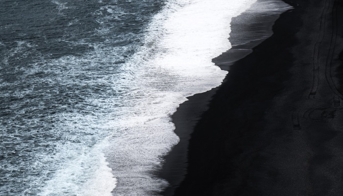 Waves crashing on a black sand beach with foamy water.