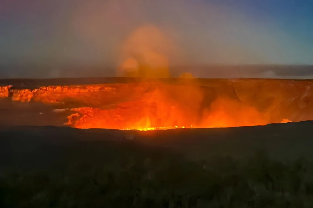 Glowing orange lava in a dark volcanic crater, emitting smoke at night.