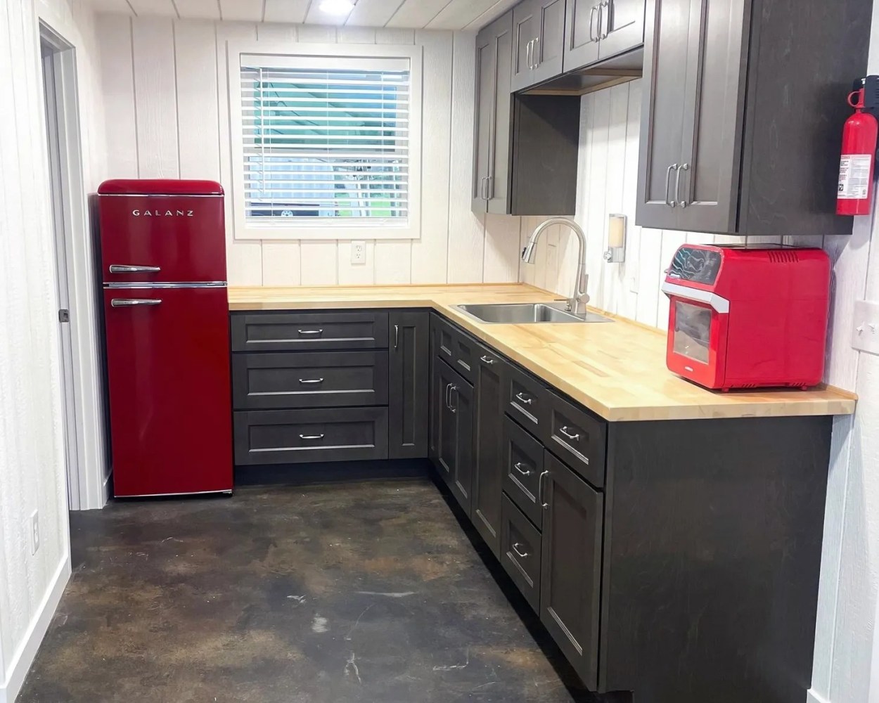 Kitchen with red fridge, gray cabinets, wood countertops, red toaster oven, and fire extinguisher.