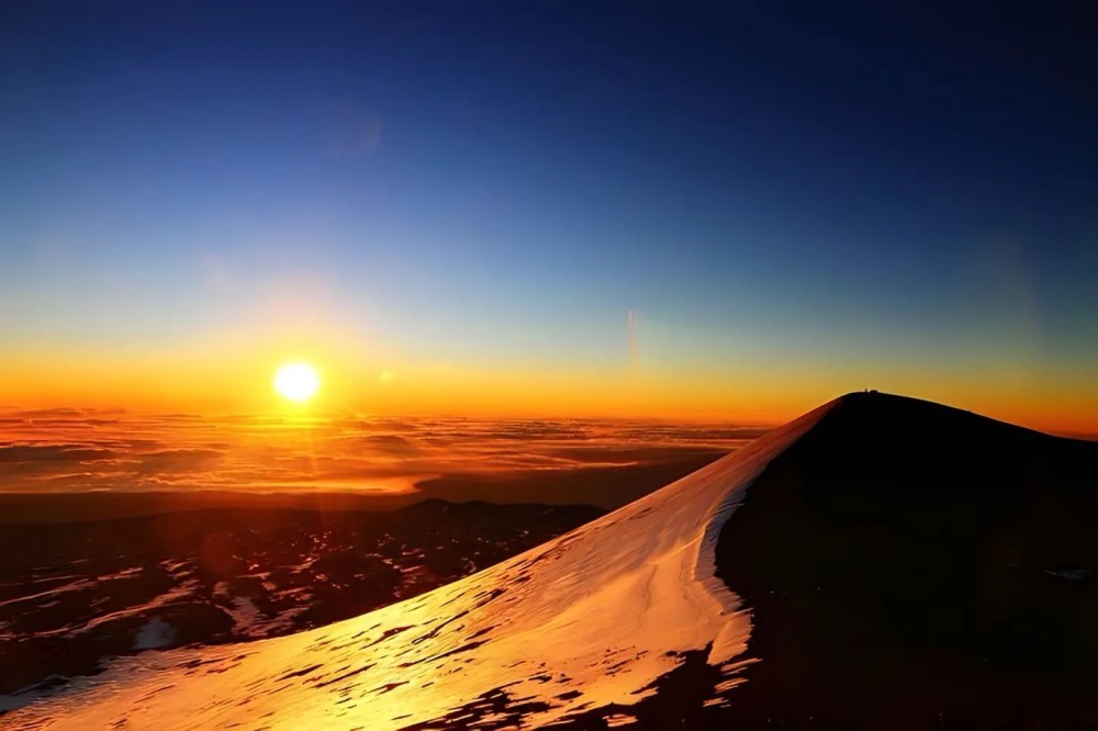 Sunset over a mountain peak with vibrant orange and blue sky.