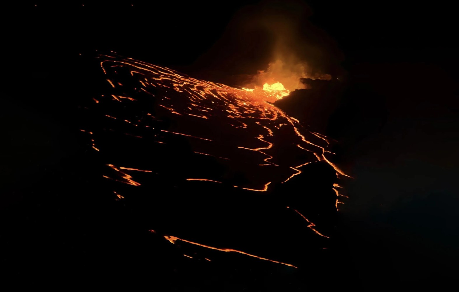 Volcanic lava glowing at night, with bright orange and black contrasts.