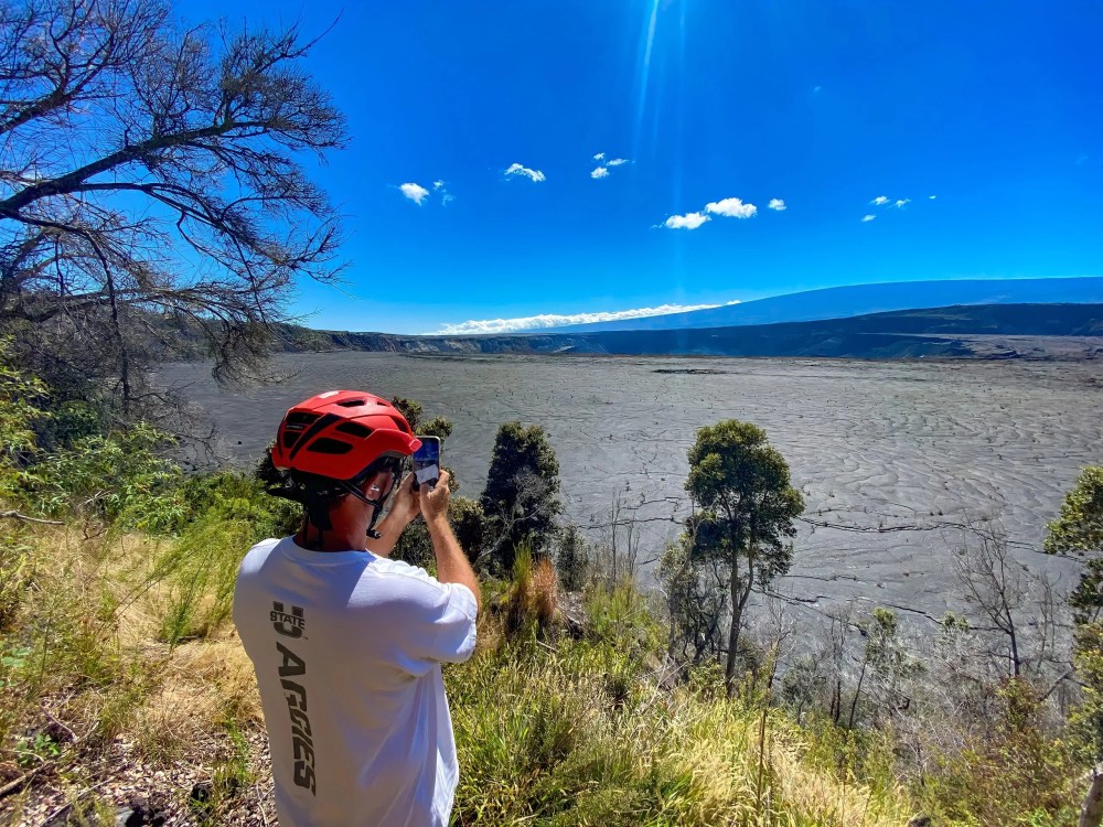 Person in red helmet taking photo of expansive dry landscape under clear blue sky.