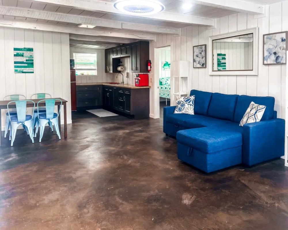 Open living area with blue sofa, dining table, and kitchenette with dark cabinets.