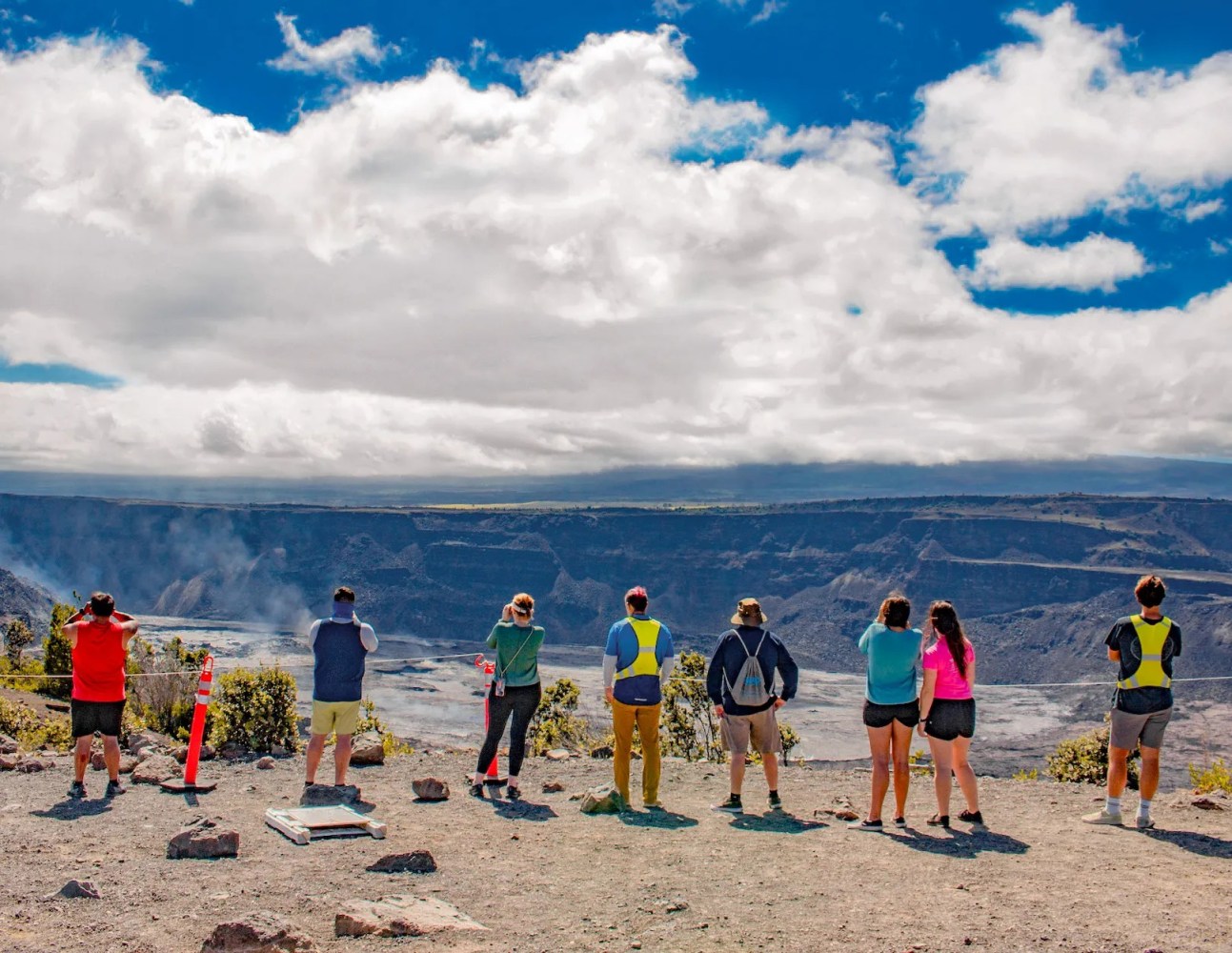 Group of people viewing a volcanic crater under a partly cloudy sky.